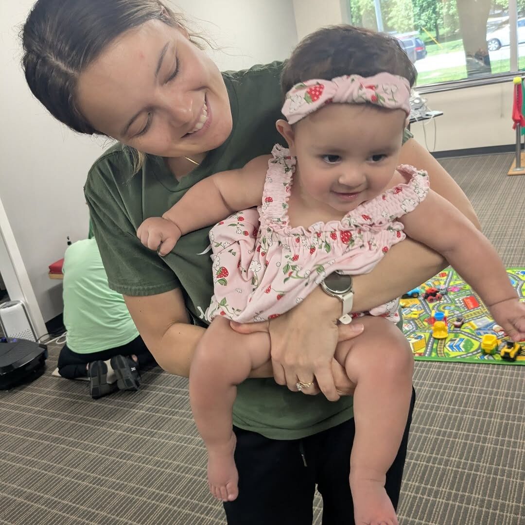 A therapist holding a smiling infant during a pediatric therapy session.