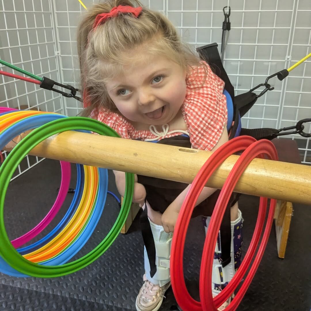 A smiling child standing and playing with colorful rings during a therapy session.